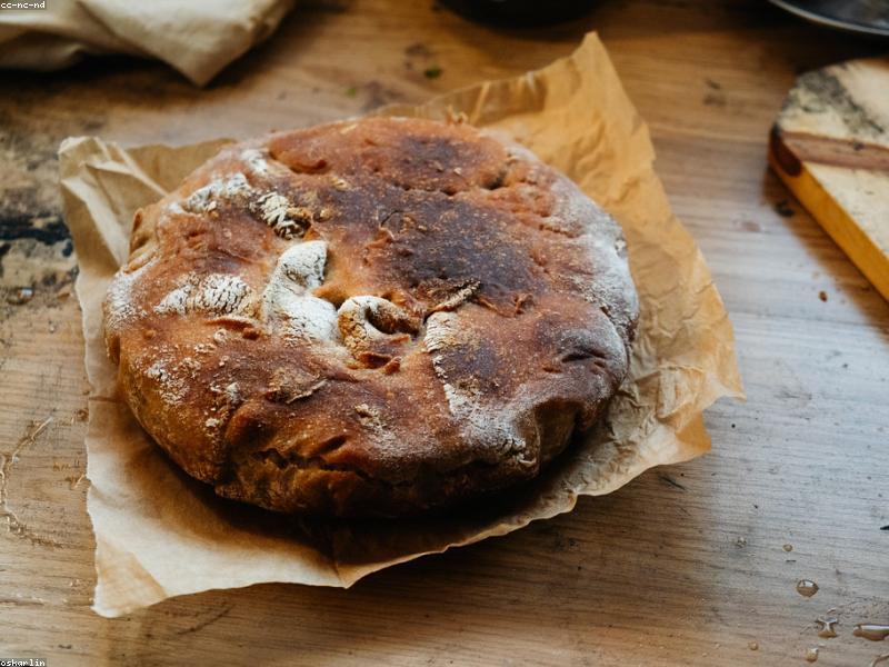 A freshly baked round sourdough loaf on a wooden cutting board with a dusting of flour