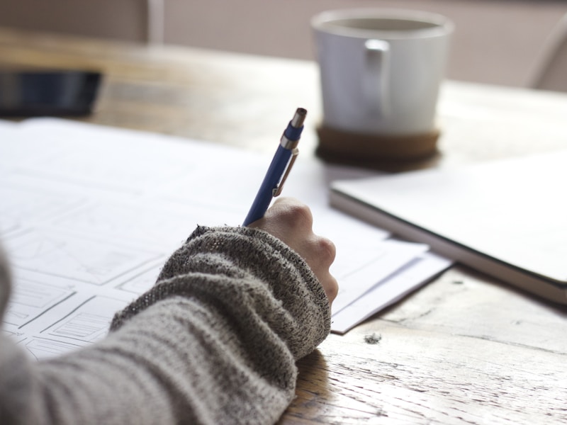 Person writing with pen on notebook for exam preparation
